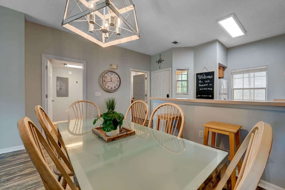 Dining area with a glass-top table and wooden chairs under a modern chandelier