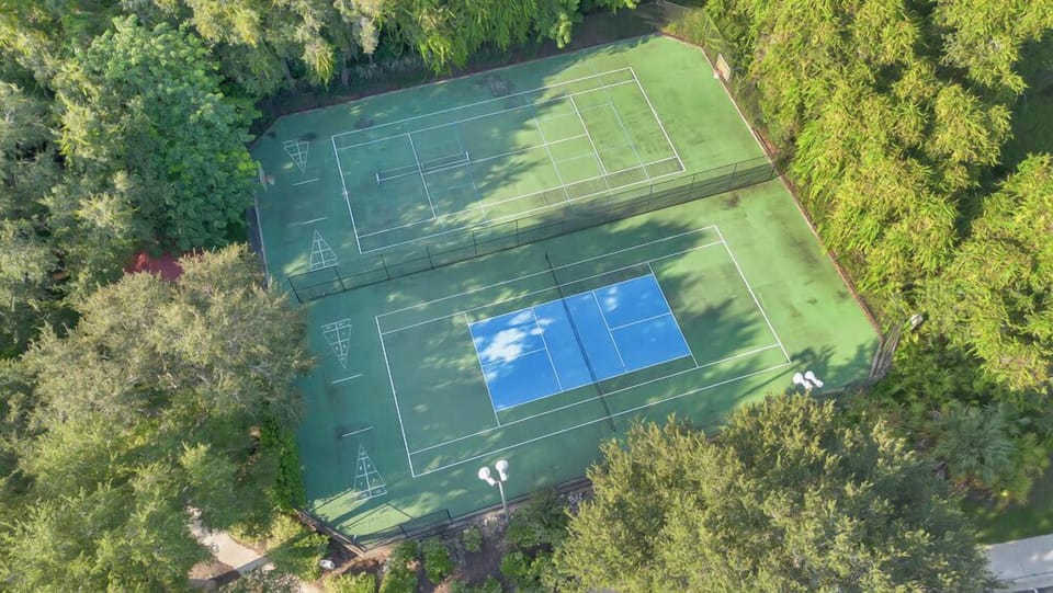 Aerial view of a tennis court surrounded by lush greenery for an active outdoor experience.