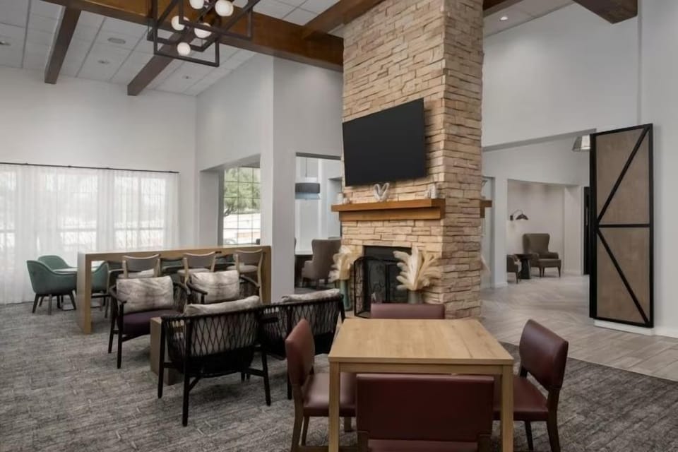 Lounge seating area with a stone fireplace, wall-mounted TV above the mantel, and wooden beam ceiling