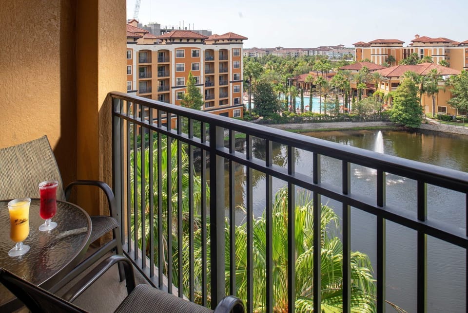 Step out to the furnished balcony overlooking the lake fountain, pool, and terracotta-roofed buildings beyond