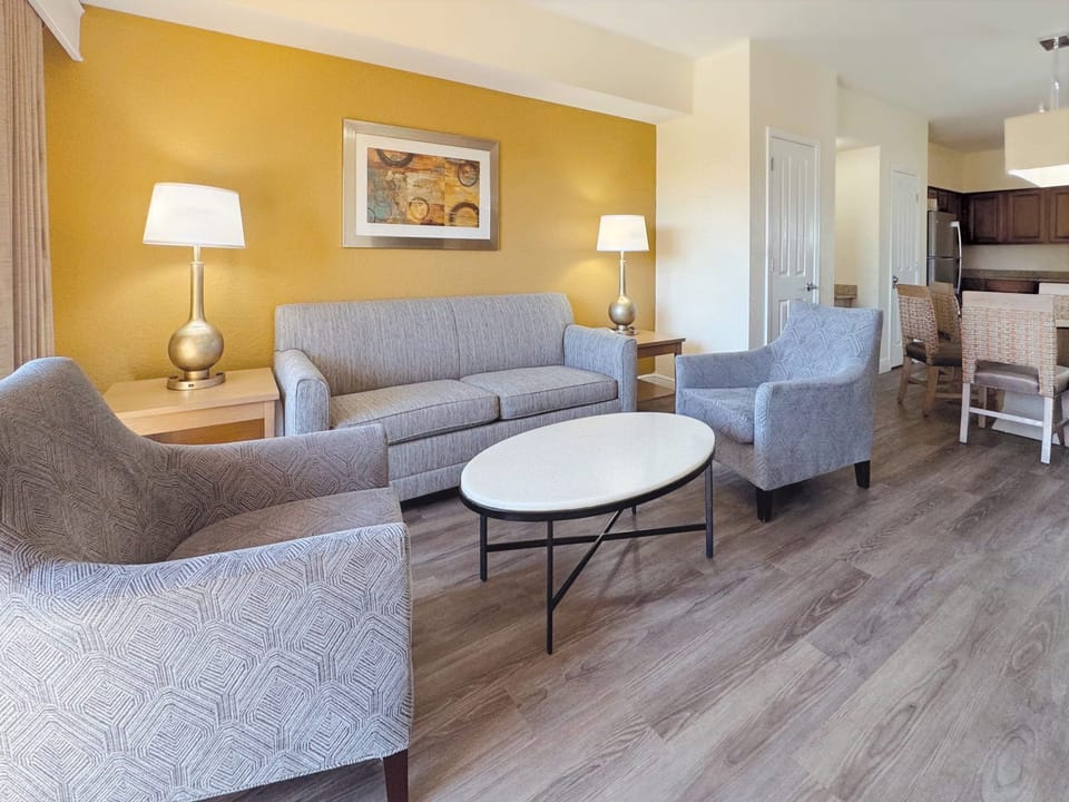 Open-plan living area with a grey sofa, accent chairs, round coffee table, and bright white walls