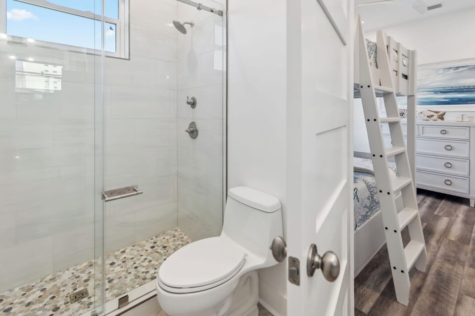 Your stylish bathroom features a spacious glass shower with mosaic tile flooring, creating a bright, modern space perfect for refreshing after beach days.