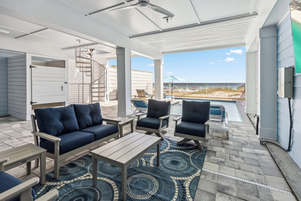 Unwind in your covered outdoor living space with plush navy seating overlooking the sparkling pool and scenic dunes beyond.