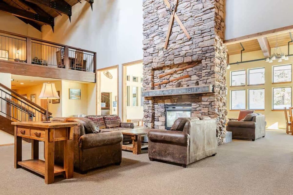Expansive common room with soaring ceilings, big windows framing meadow and red cliff views—cozy seating, stone fireplace, and rustic charm throughout.