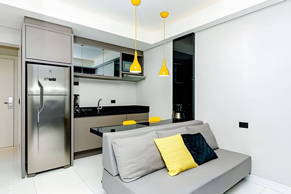 Cozinha/Sala com sofá 3 lugares, balcão 2 lugares, micro-ondas, pia, armários e geladeira.