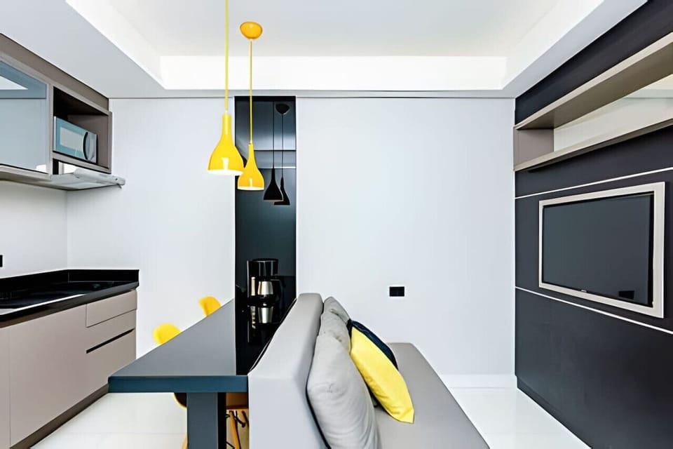 Sala/Cozinha - sofá 3 lugares, micro-ondas, balcão 2 cadeiras, armários e televisão.