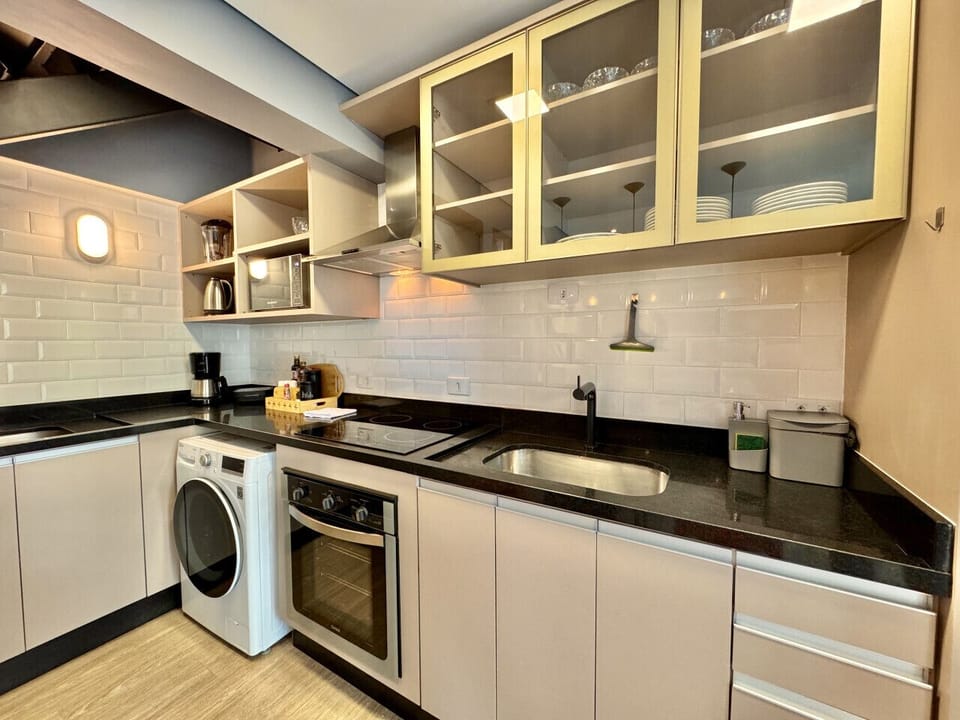 Cozinha com cooktop 4 bocas, pia, rodo de pia, armários, pratos, tigelas, micro-ondas, cafeteira, exaustor e máquina de lavar.