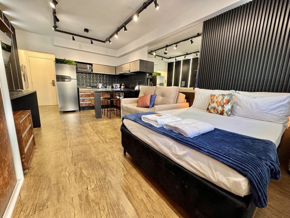 Studio com cama de casal, sofa bege e painel ripado preto