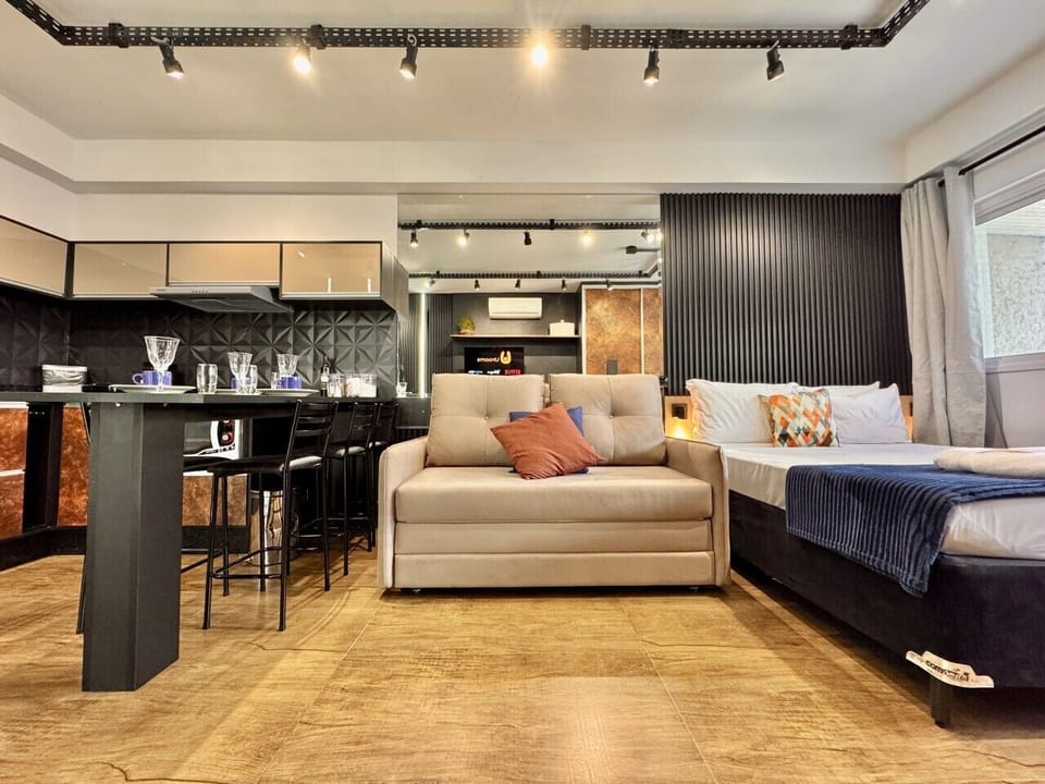 Cama de casal com edredom azul marinho e sofa bege na sala