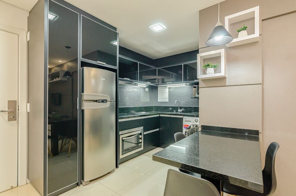Cozinha moderna e completa com geladeira, forno, cooktop 4 bocas, exaustor, pia, armários, lava e seca, micro-ondas e balcão 3 lugares.
