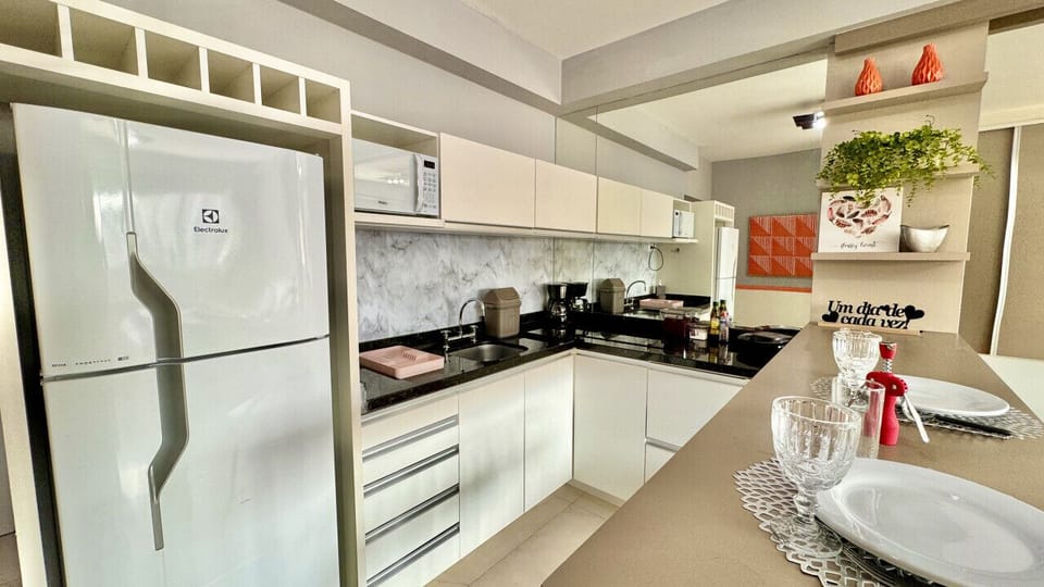 Cozinha com geladeira branca, fogao, bancada e bancos altos
