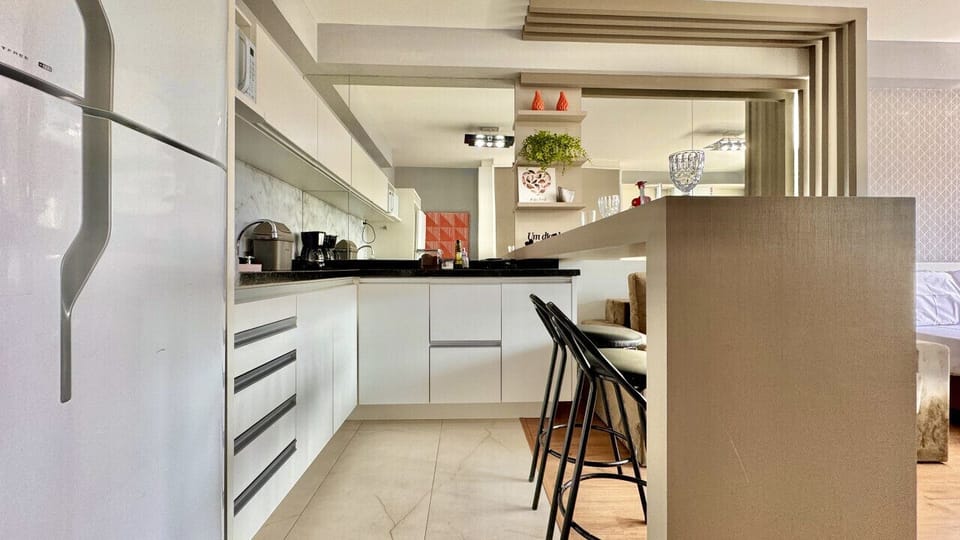Cozinha com bancada, armarios brancos, geladeira, fogao e cadeiras