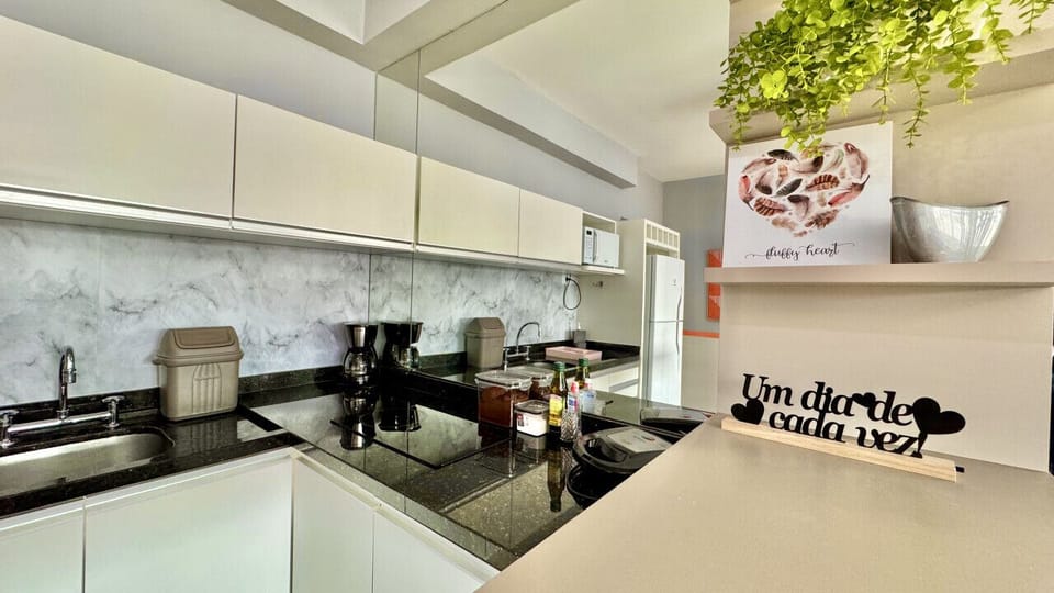 Cozinha com bancada preta, fogao, geladeira inox e decoracoes