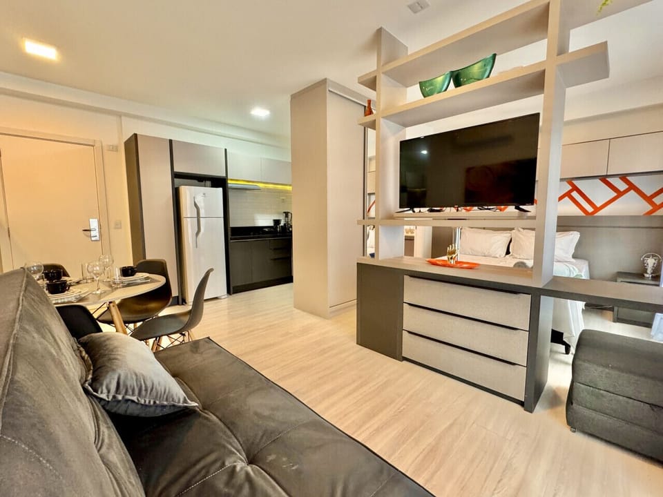 Sala integrada com sofa cinza, TV e cozinha aberta ao fundo