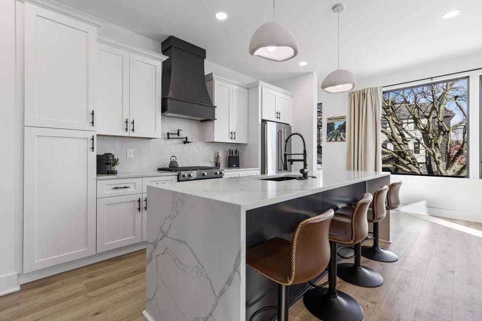 Kitchen with an island that doubles as a hangout spot. Waterfall countertop, bar stools, and a full stove mean the cook stays connected to the conversation and the group