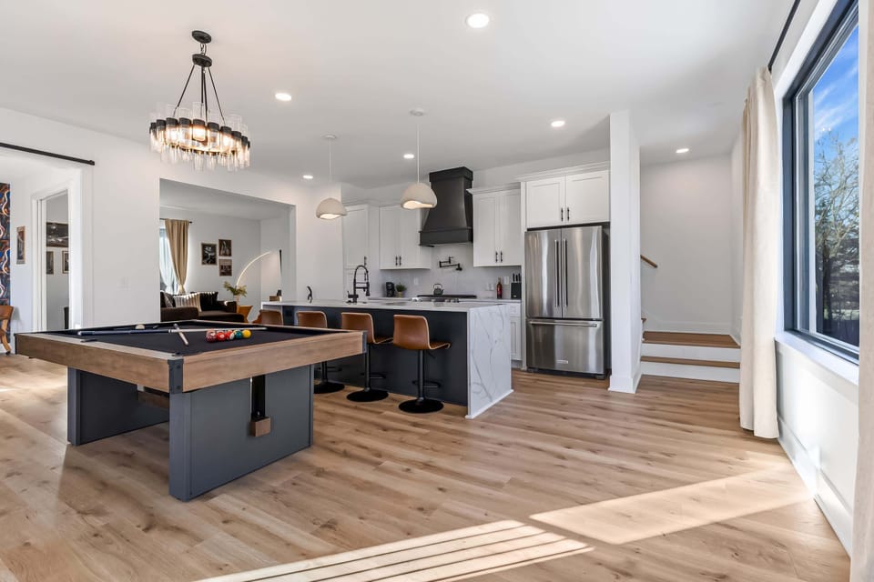 Pool table flows straight into the kitchen island where the group plays and cooks at once, no one stuck watching from the sidelines