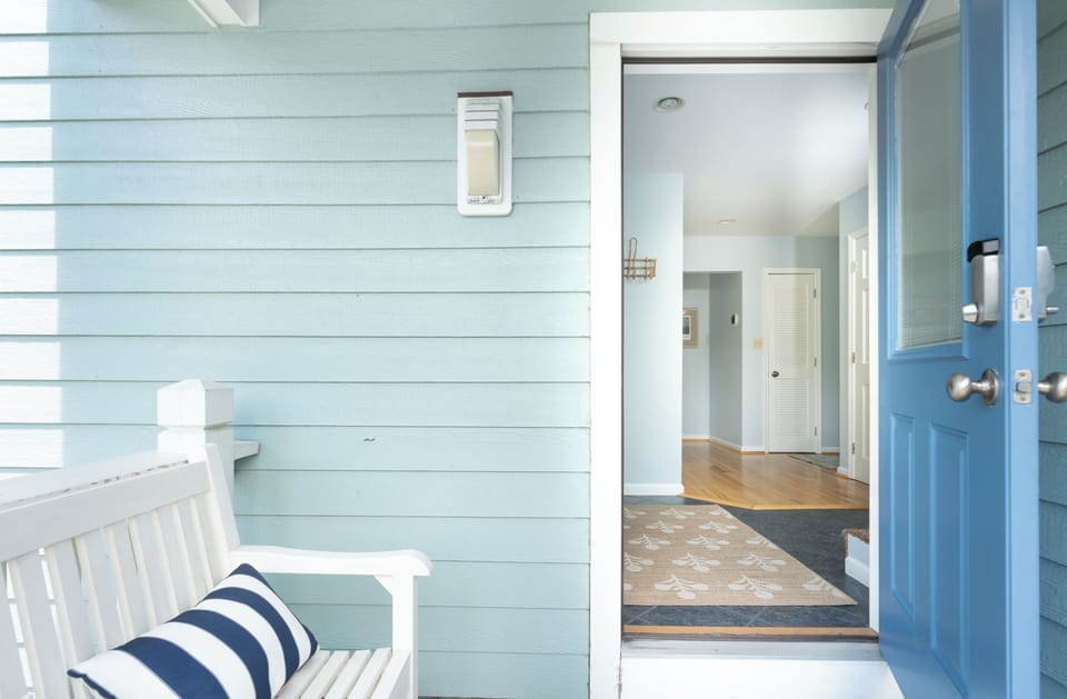 This charming beach cottage entrance welcomes you with soft coastal blues and crisp white accents. The open doorway reveals a bright, airy interior with hardwood floors that invite you in.