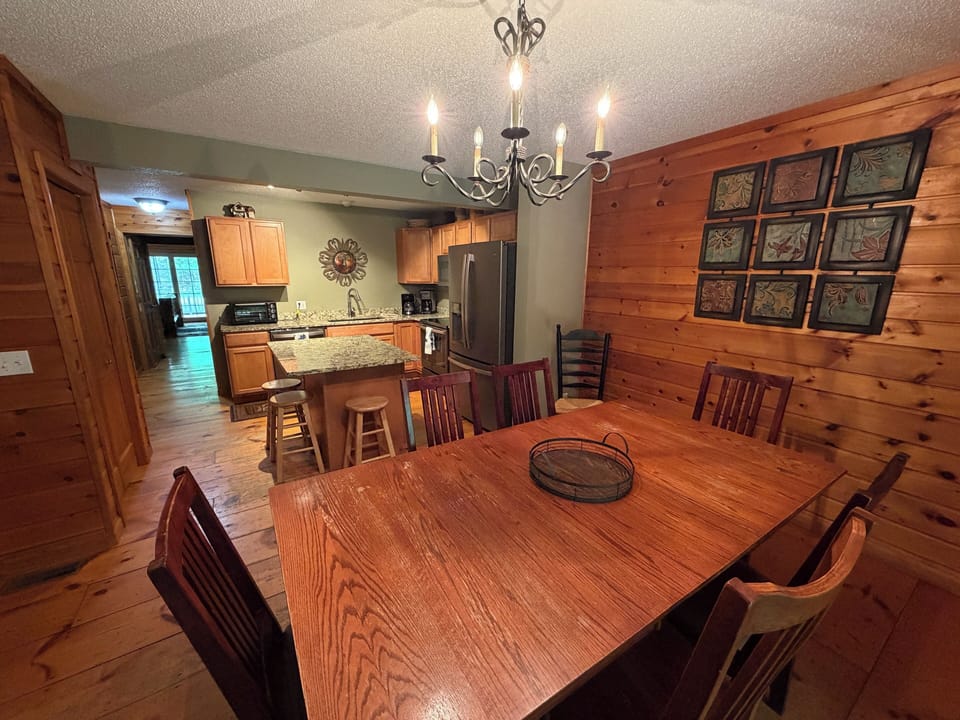 Gather your group around the rustic wood table, lit by warm chandelier glow, with a fully-equipped kitchen ready for home-cooked meals and easy conversation in this cozy cabin retreat.