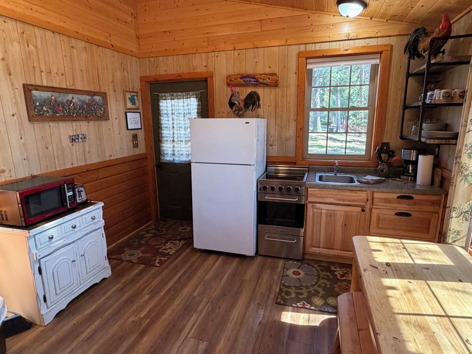 Step into your cozy cabin kitchen, where rustic charm meets convenience with full-size appliances, warm wood surroundings, and sunlight streaming through the windows—perfect for preparing home-cooked meals.