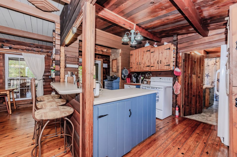 Cook up comfort in this rustic log cabin vacation rental featuring a charming full kitchen, cozy bar seating, and warm wood finishes—perfect for culinary adventures during your relaxing family retreat or countryside getaway.