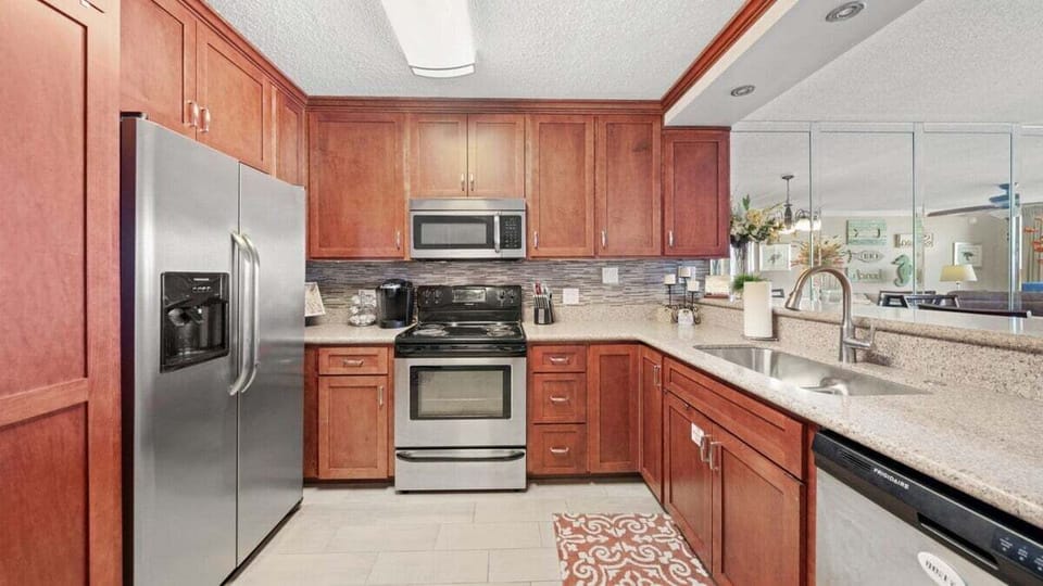 Full kitchen with wood cabinetry, stainless appliances, and sleek tile backsplash—ideal for beachside cooking.