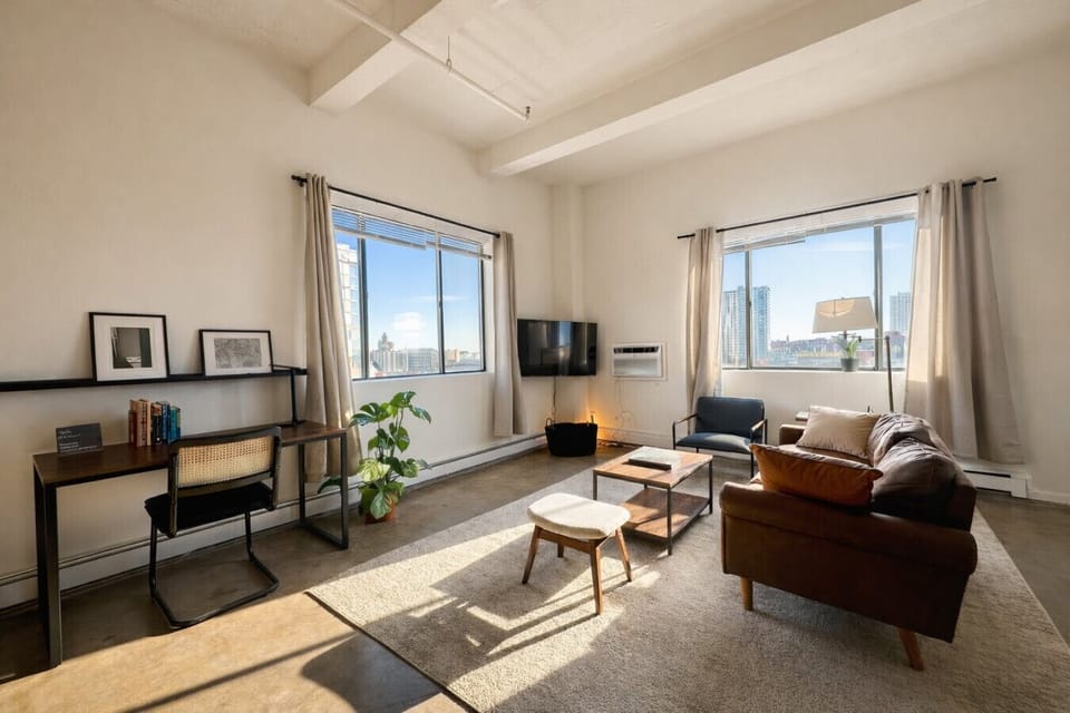 Welcome to your sun-drenched corner studio, featuring a plush queen bed and wall-to-wall windows.