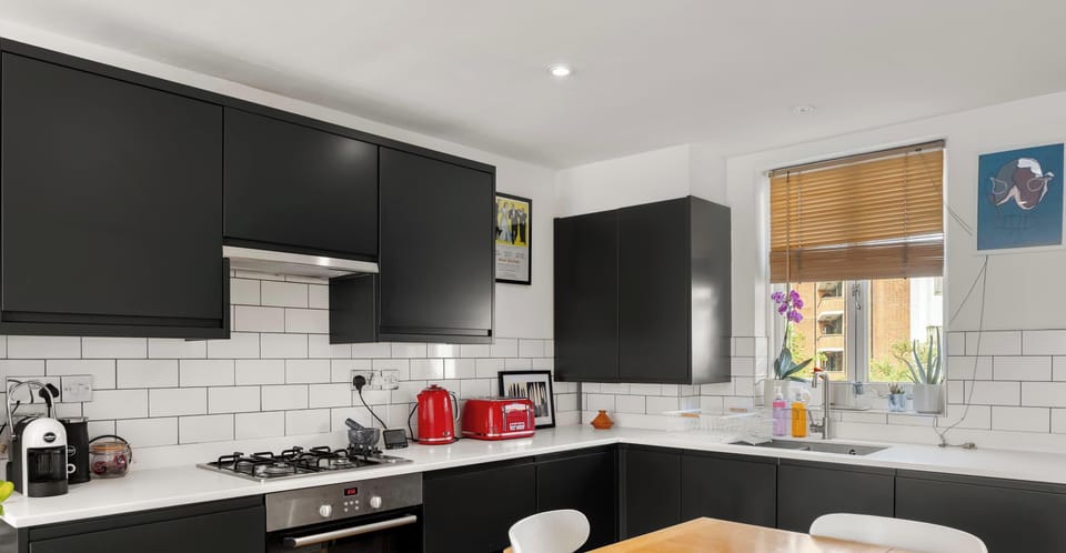 This stylish modern kitchen makes a bold statement with its sleek matte black cabinetry and contrasting white countertops. The clean white subway tile backsplash adds a classic touch, while the vibrant red appliances, including a matching kettle.