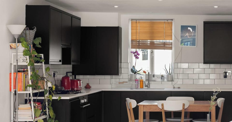 This stylish modern kitchen makes a bold statement with its sleek matte black cabinetry and contrasting white countertops. The clean white subway tile backsplash adds a classic touch, while the vibrant red appliances, including a matching kettle.