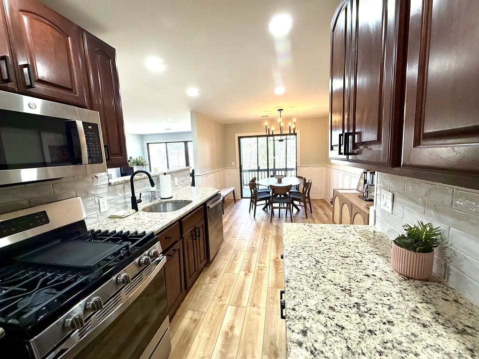 Bright, modern kitchen featuring granite countertops, new stainless steel appliances, and stunning views of the surrounding tree canopy—perfect for cooking and connecting.