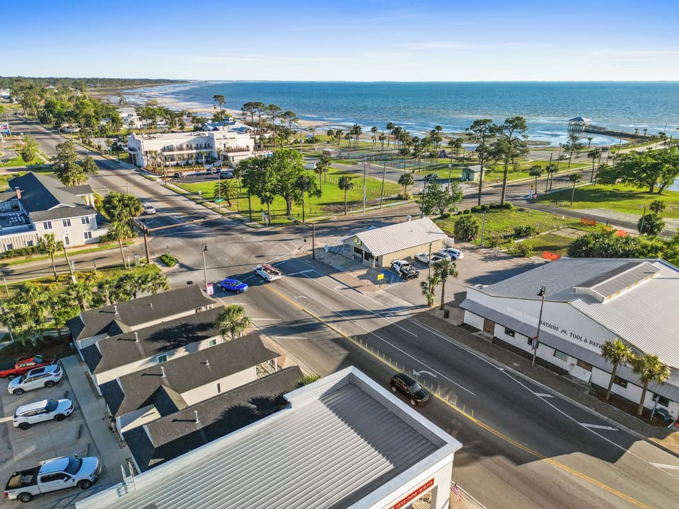 Aerial view of coastal town featuring beautiful beachfront area with palm trees, local businesses, and waterfront pier stretching into blue waters.