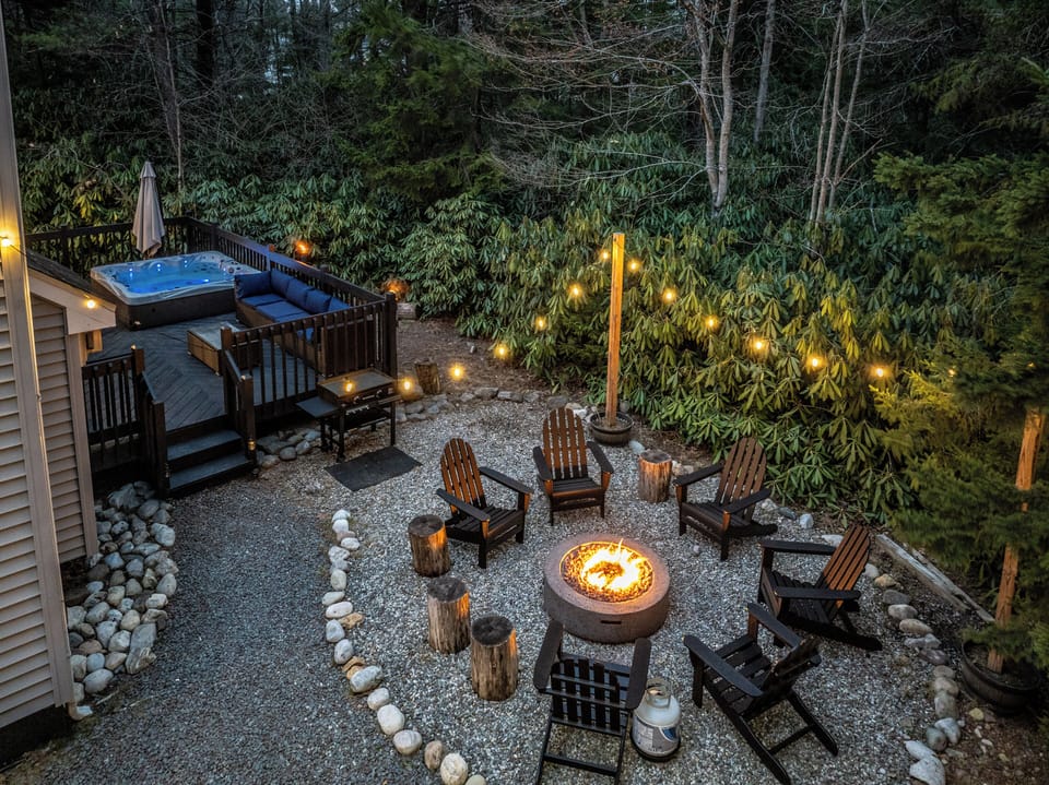 Relax on the deck with a glowing hot tub and comfy seating, surrounded by lush greenery. Enjoy the gravel courtyard’s fire pit, Adirondack chairs, and string lights for a warm evening under the stars.