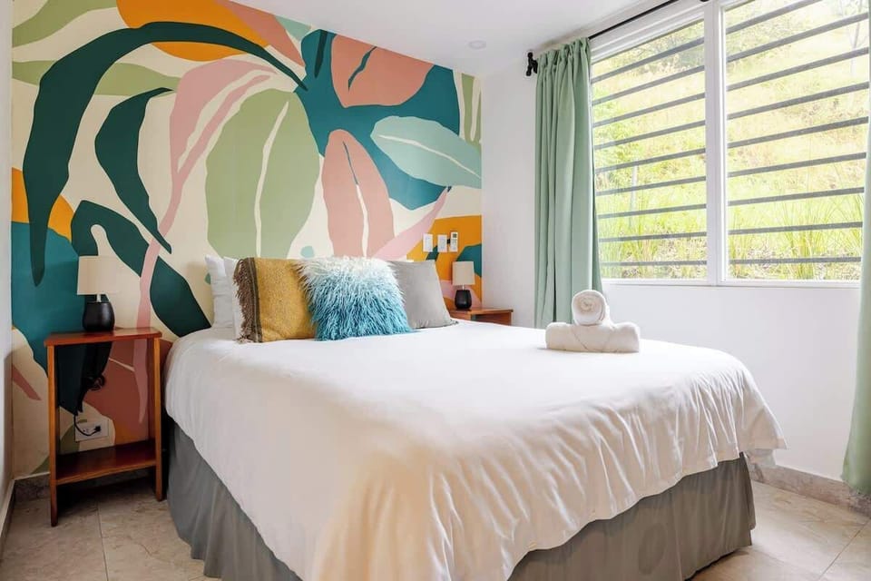 Studio 102 – First Floor
With a queen bed and a comfy sofa bed, this studio combines simplicity with comfort. Floor-to-ceiling glass doors let in natural light, while tropical prints add a playful design touch.