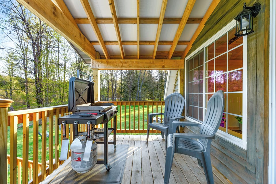 Covered porch with BBQ grill and forest view seating.