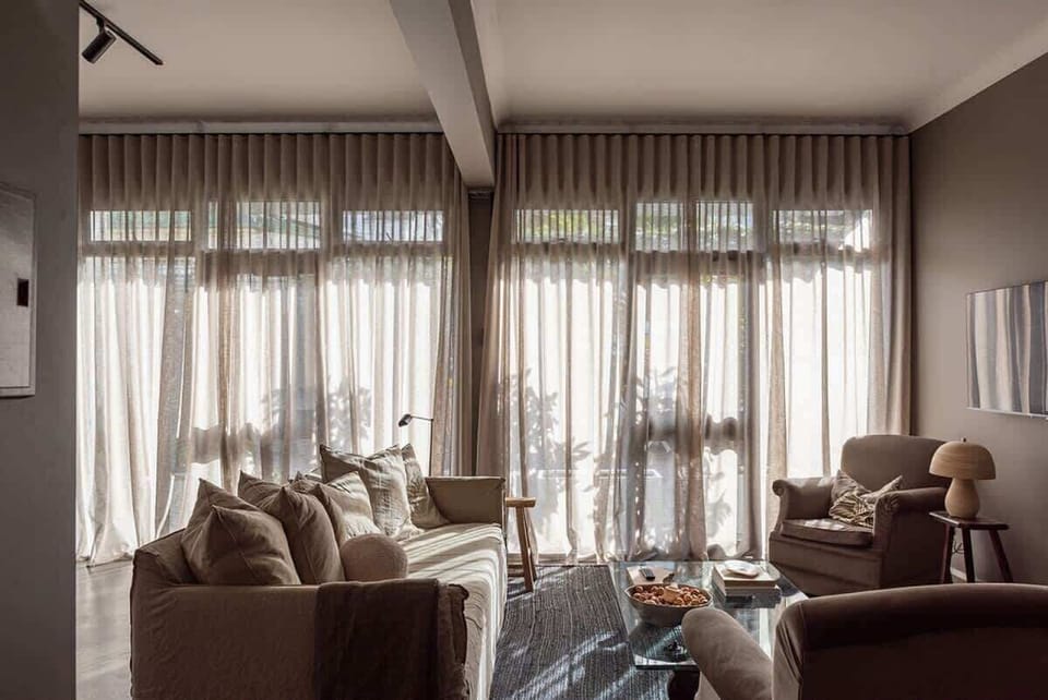 Vintage armchairs covered in soft velvet, a comfortable linen sofa and sunlight curtains form a warm, inviting space.