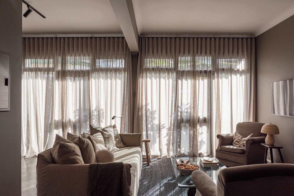 Vintage armchairs covered in soft velvet, a comfortable linen sofa and sunlight curtains form a warm, inviting space.