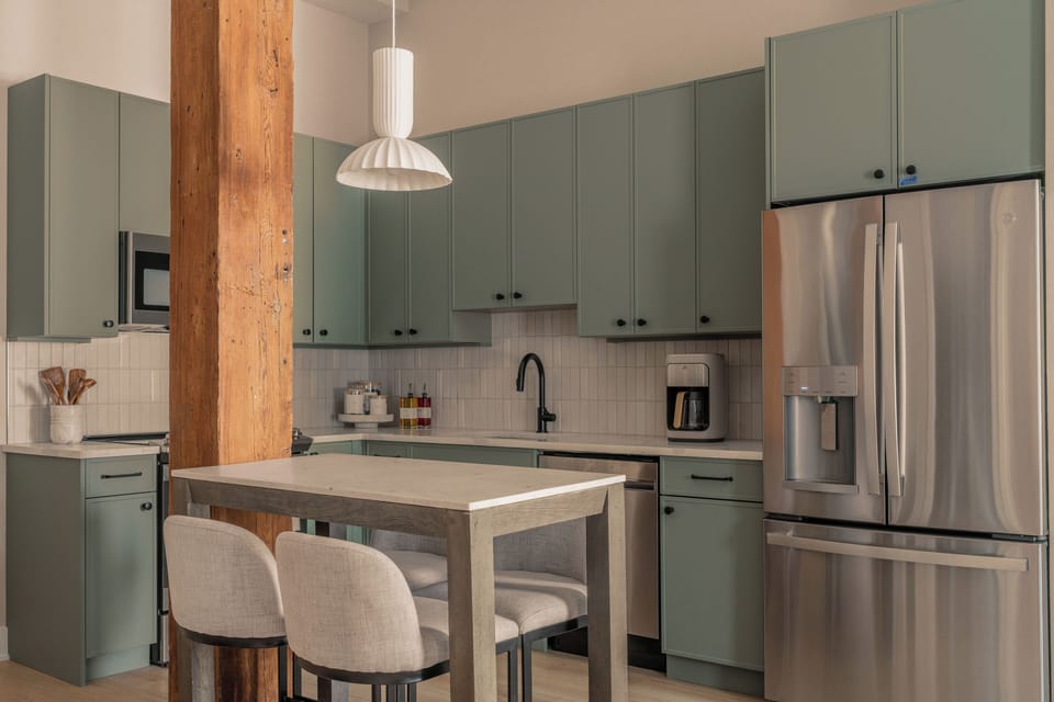 Kitchen view with green cabinets, white pendant and sleek island.