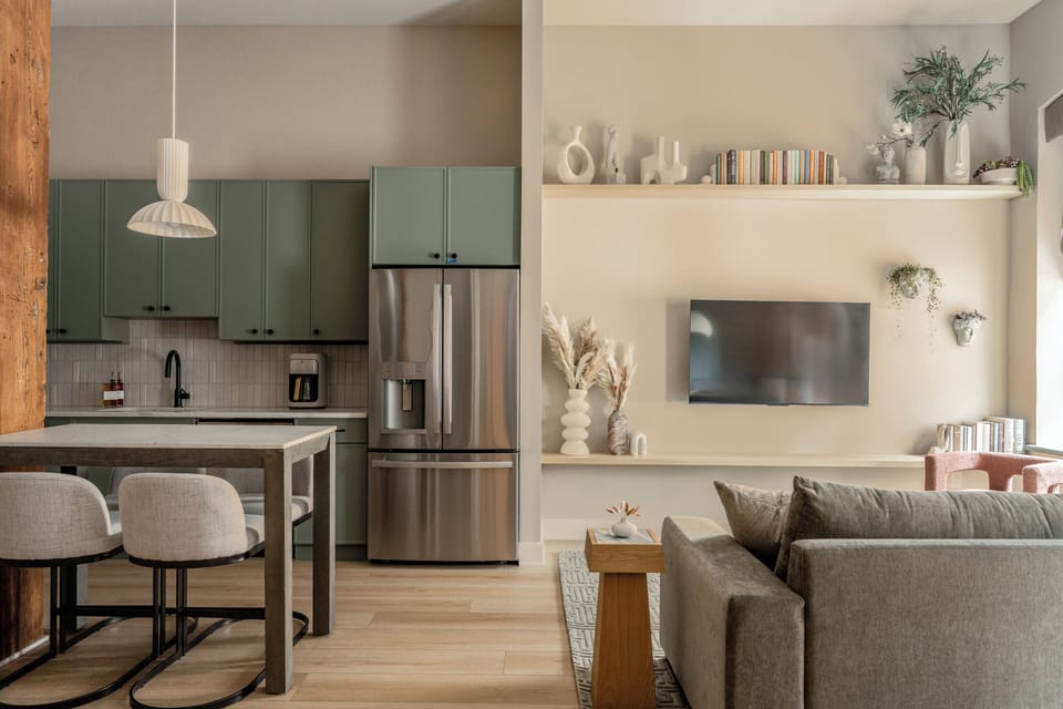 View of kitchen/living area, blending green cabinets, TV, and custom shelving.