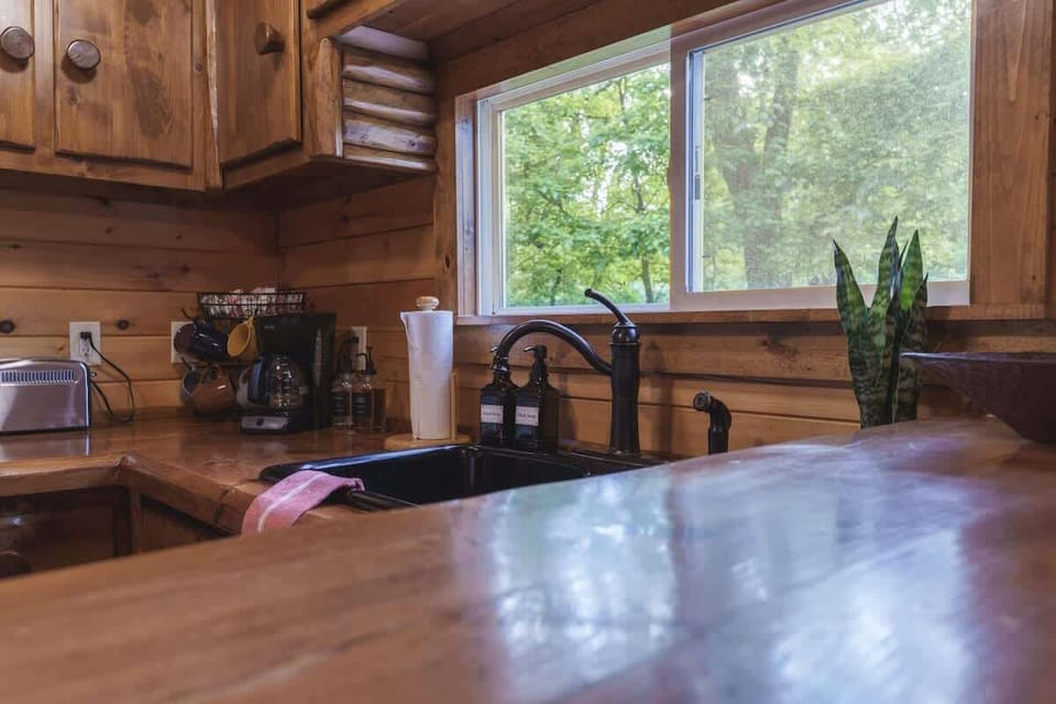 Rustic kitchen sink beneath a wide window, offering peaceful views of the surrounding trees while you cook