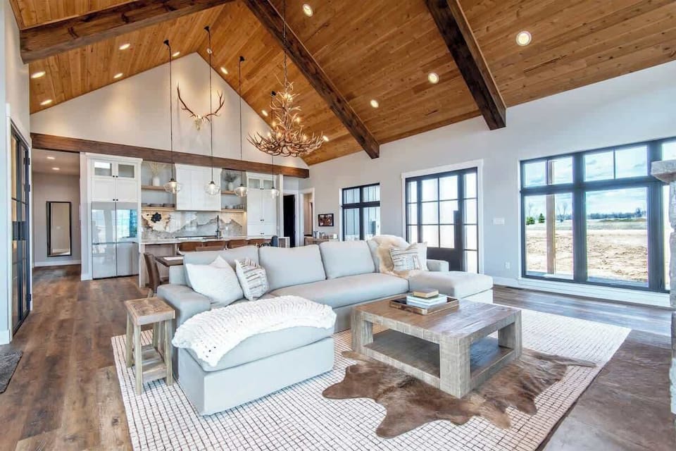 The great room's full sweep — timber beams, stone, and glass working together to frame one of the most dramatic interior spaces in Teton Valley.