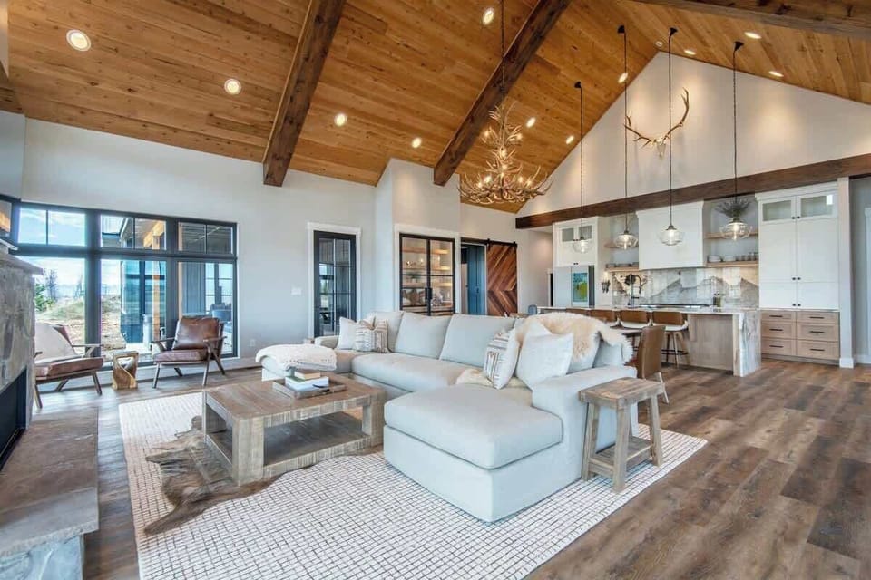 Open-plan great room from a wider angle — kitchen, dining, and living all flowing under cathedral ceilings with the Tetons pulling focus through every window.