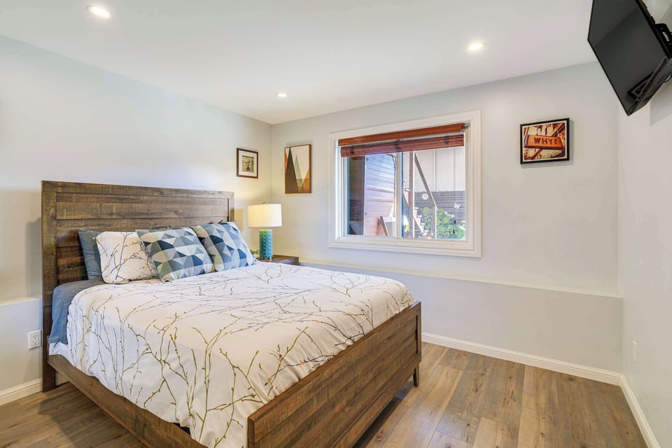 Unwind in this bright and airy bedroom featuring a rustic wood bed frame, soft neutral tones, and natural light streaming through the window for a peaceful night’s rest