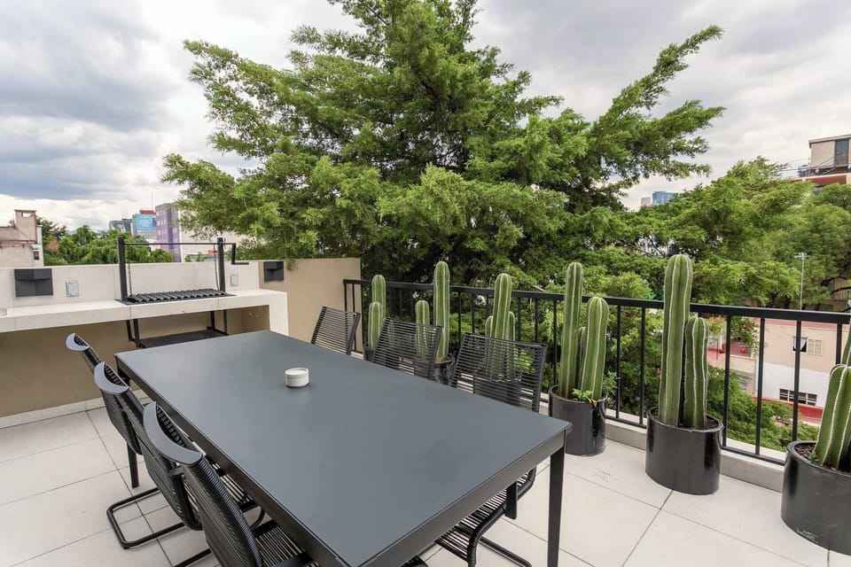 Terraza común ubicada en el quinto piso, cuenta con zona de asador de carbón y comedor exterior, así como sillas de estar. Disfruta la vista a la ciudad y sus hermosos atardeceres
