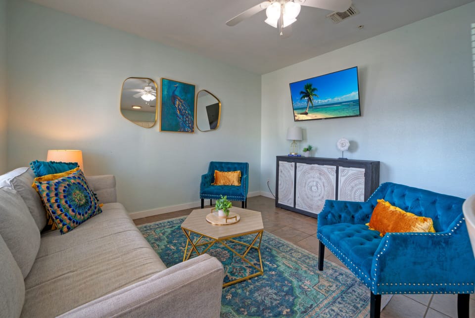 A bright condo living room with coastal accents, comfortable seating, and a TV.
