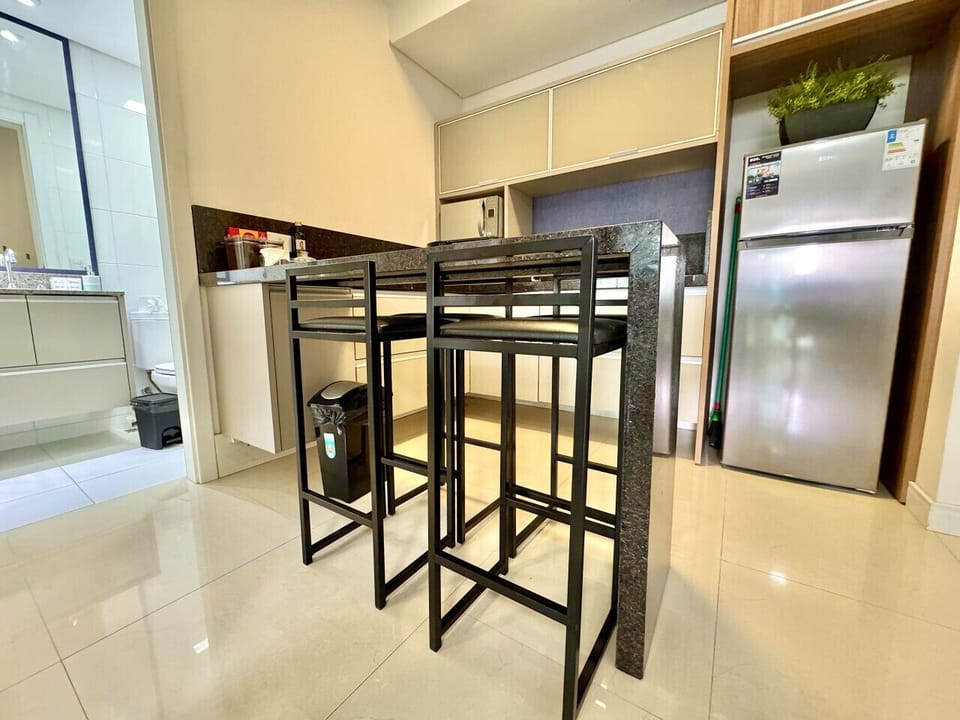Cozinha compacta com balcao, geladeira inox, cadeiras altas pretas.