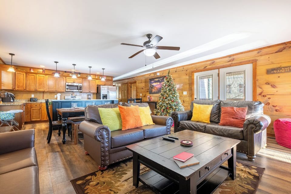 Relax in this cozy open-concept living space with leather seating, colorful pillows, and rustic wood walls that create the perfect holiday retreat.