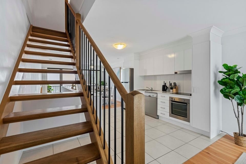 Open-plan living with ceiling fan, seating, TV and lounge by the stairs.