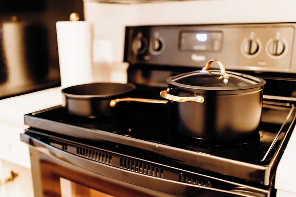 Sleek black cookware with golden handles sits ready on a gleaming stovetop, inviting cozy nights in and warm meals made with love. Whether you're whipping up a quick breakfast or simmering something special, the kitchen is stocked and stylishly set.
