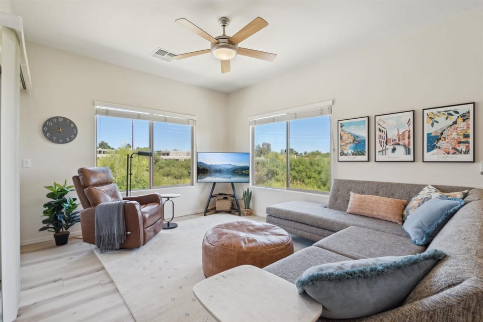 The Living Room is a bright space with plush seating, a Smart TV, and peaceful green views through large windows.