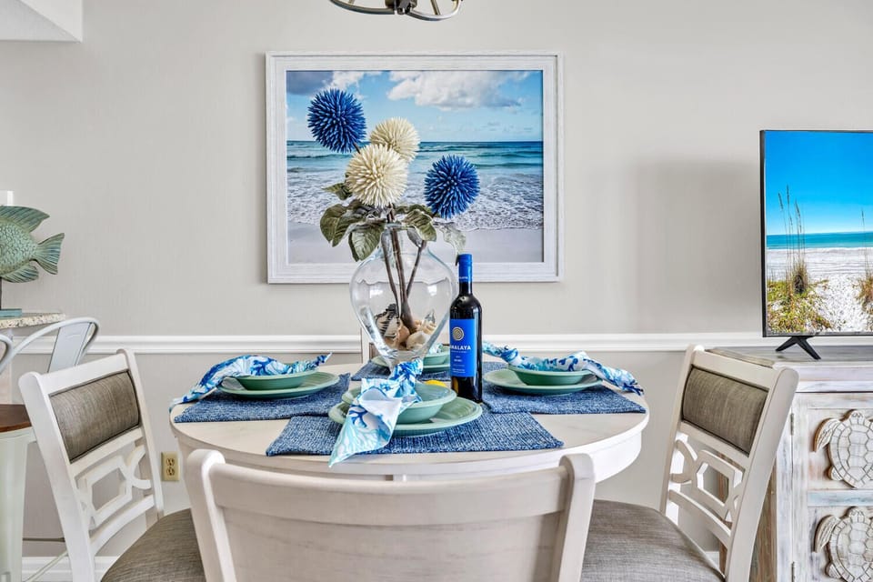 Your elegant dining table awaits with coastal charm, featuring beautiful blue accents and beachy artwork that captures the seaside spirit perfectly.