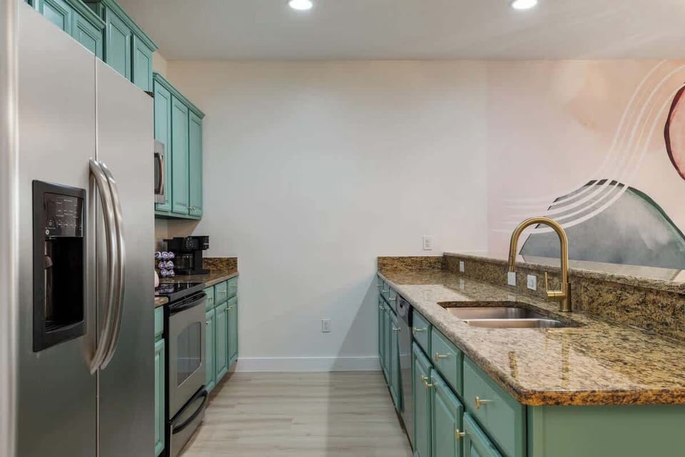 Stylish kitchen with stainless steel appliances, teal cabinets, and granite countertops. Perfect for cooking and entertaining. Experience modern comfort—book your stay now!